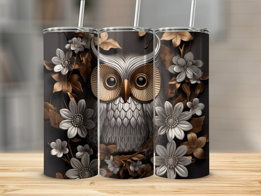 Owl with gold eyes surrounded by metallic leaves and white flowers on a dark tumbler.