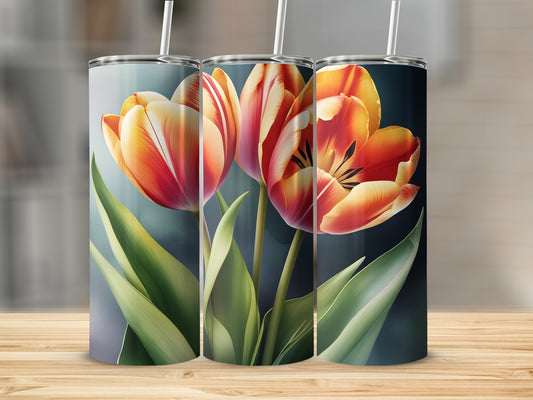 Three tulips in orange and red hues with green leaves on a tumbler.