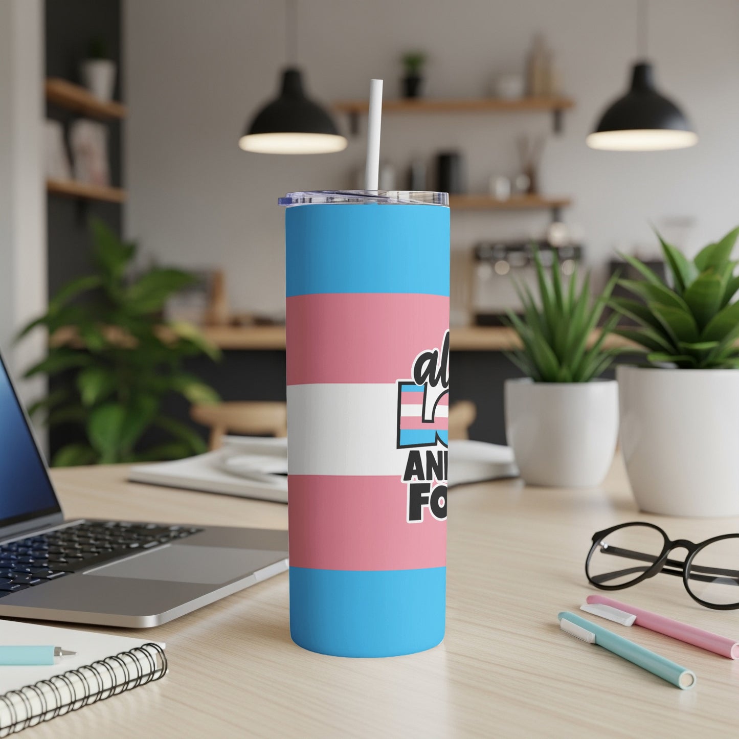 Transgender pride flag tumbler on a desk with a laptop and pens.