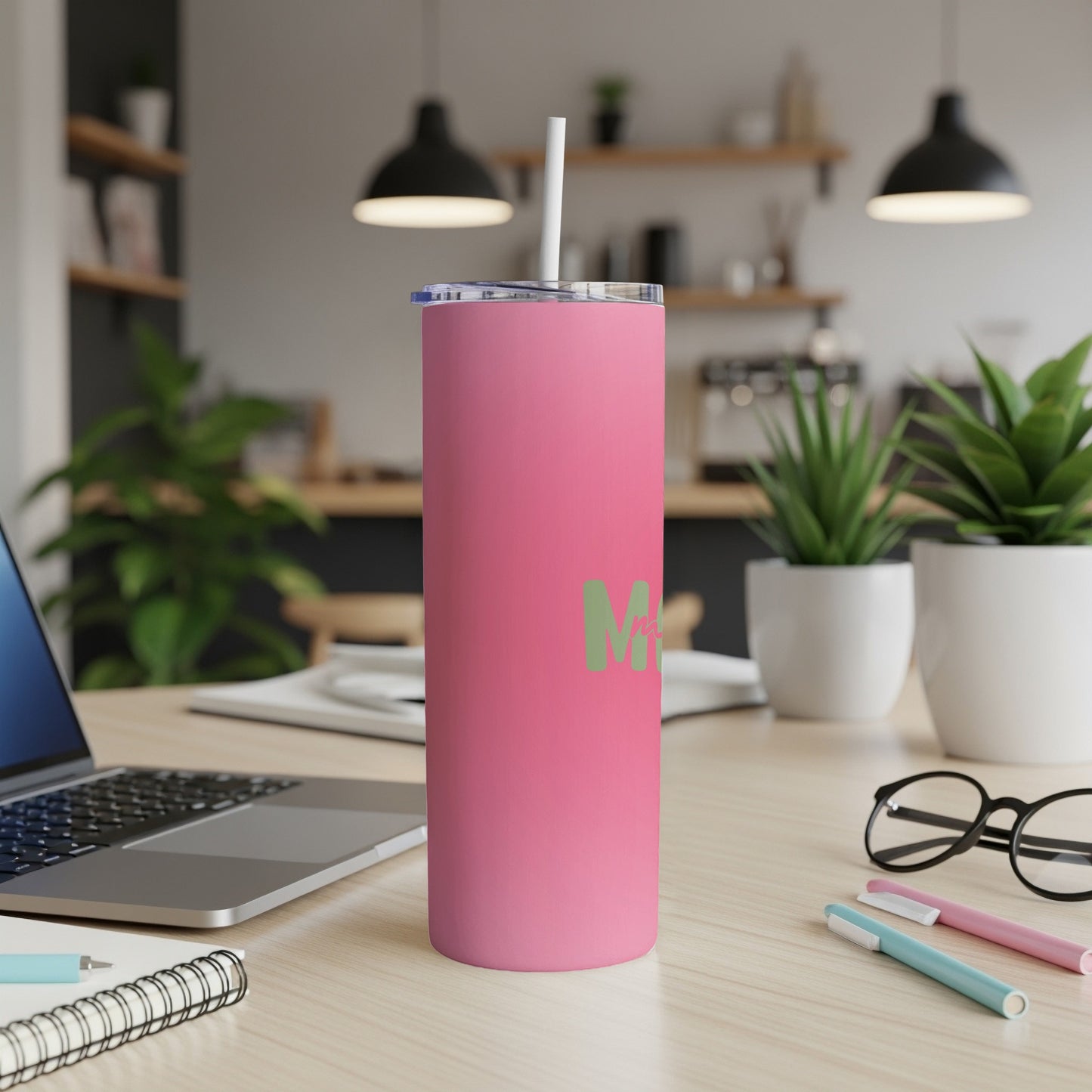 Pink tumbler with a light green "M" logo, on a desk with a laptop.