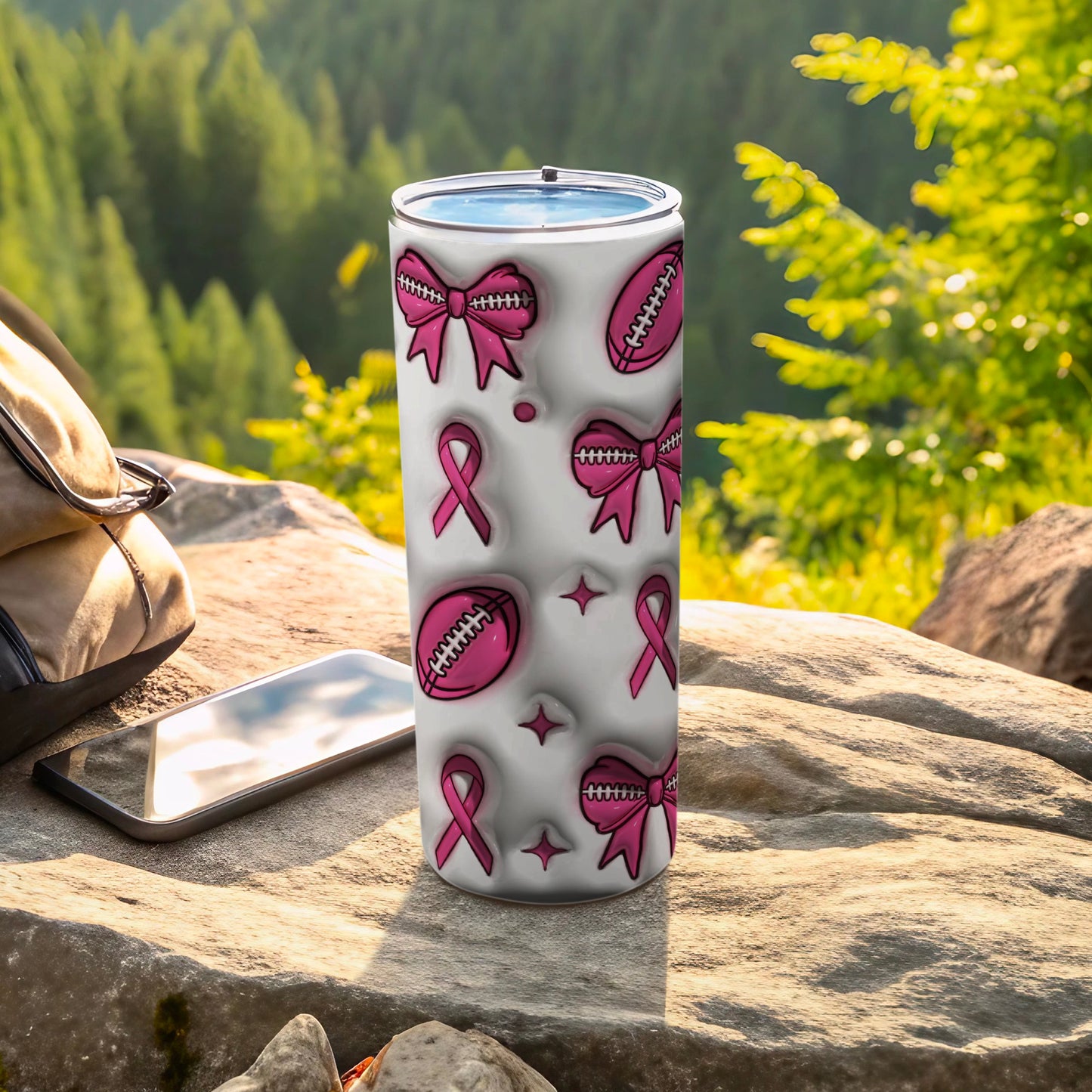 Tumbler with pink ribbon and football patterns on a rock.