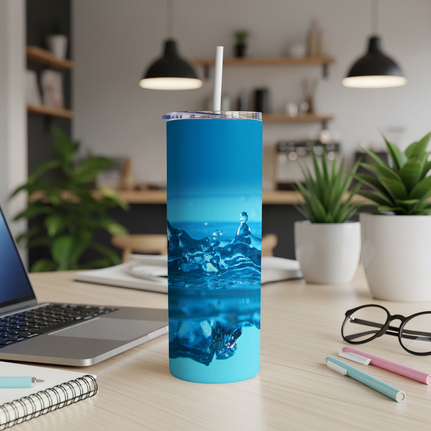Blue insulated tumbler with white straw on desk next to laptop and pens.