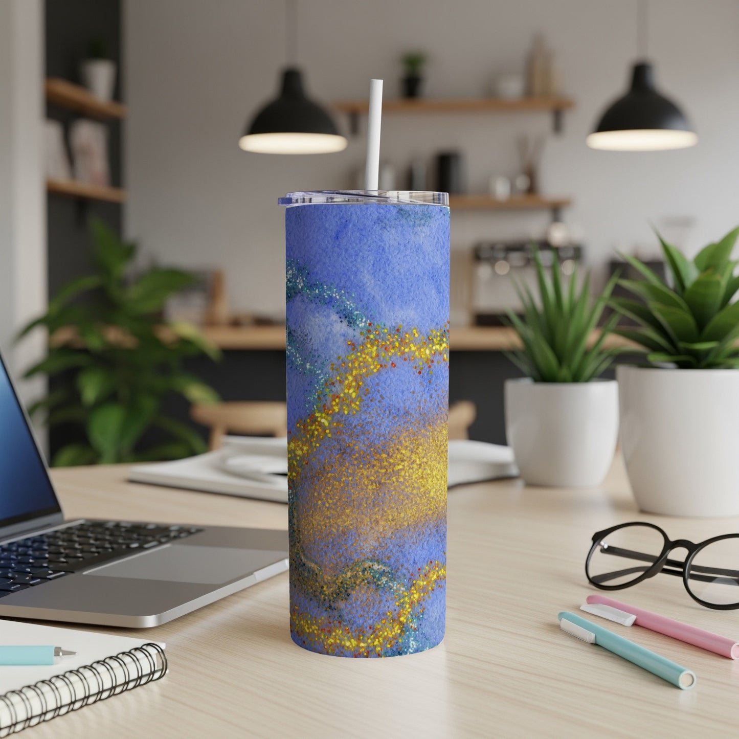 Blue tumbler with gold glitter and watercolor swirls on a desk.
