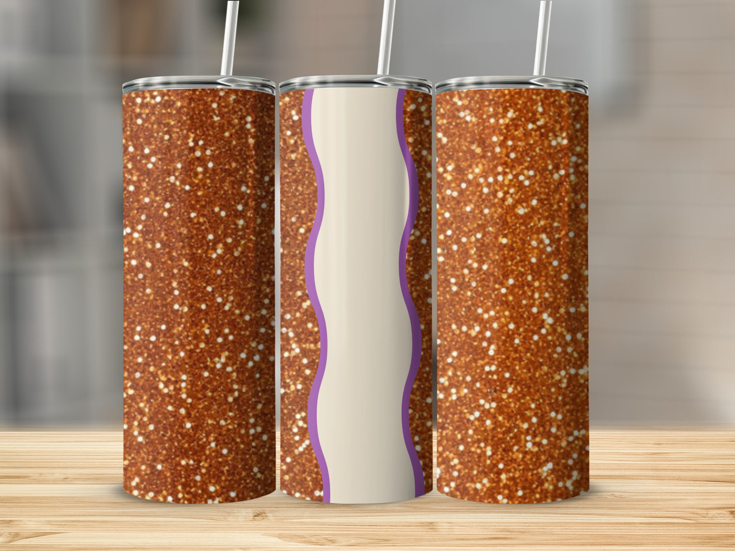 Three glitter-covered tumblers with straw on a wooden surface.