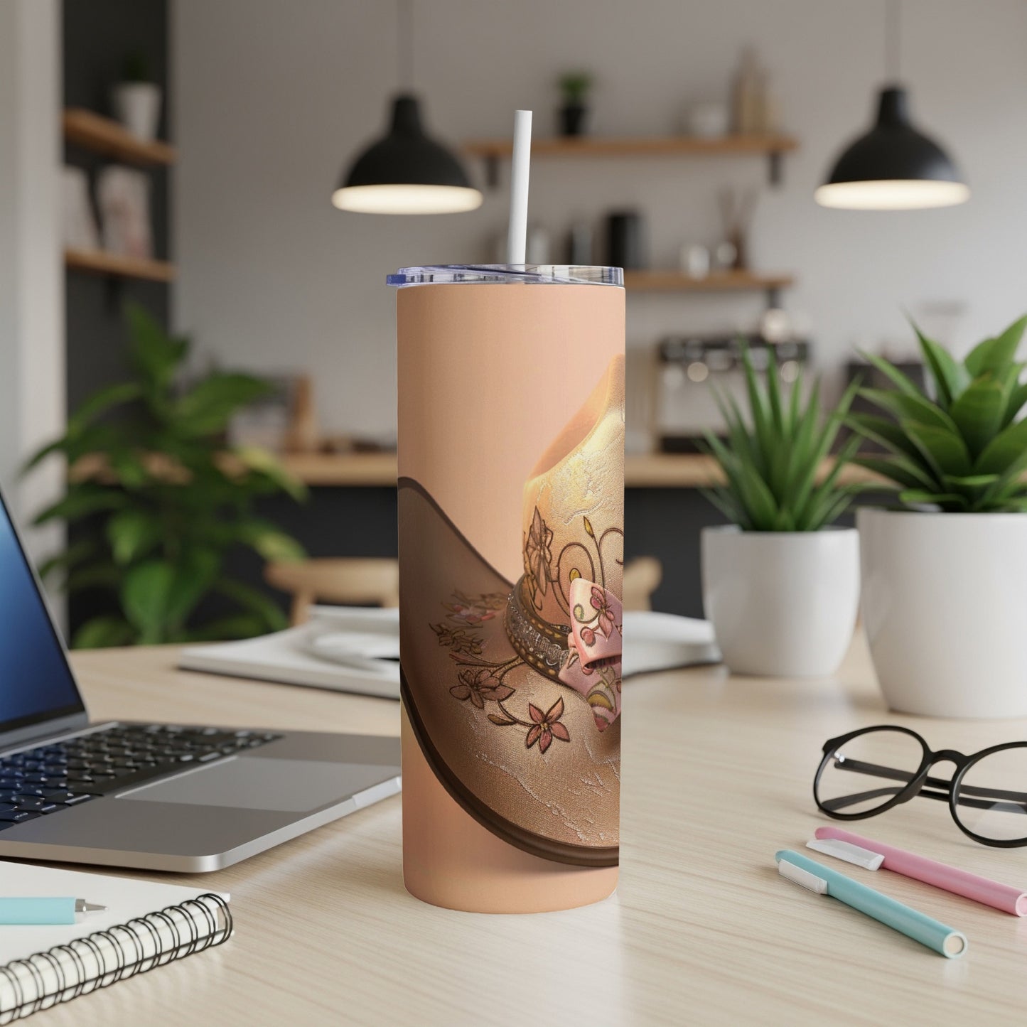 Cowboy hat design on a tall, tan tumbler with a straw.