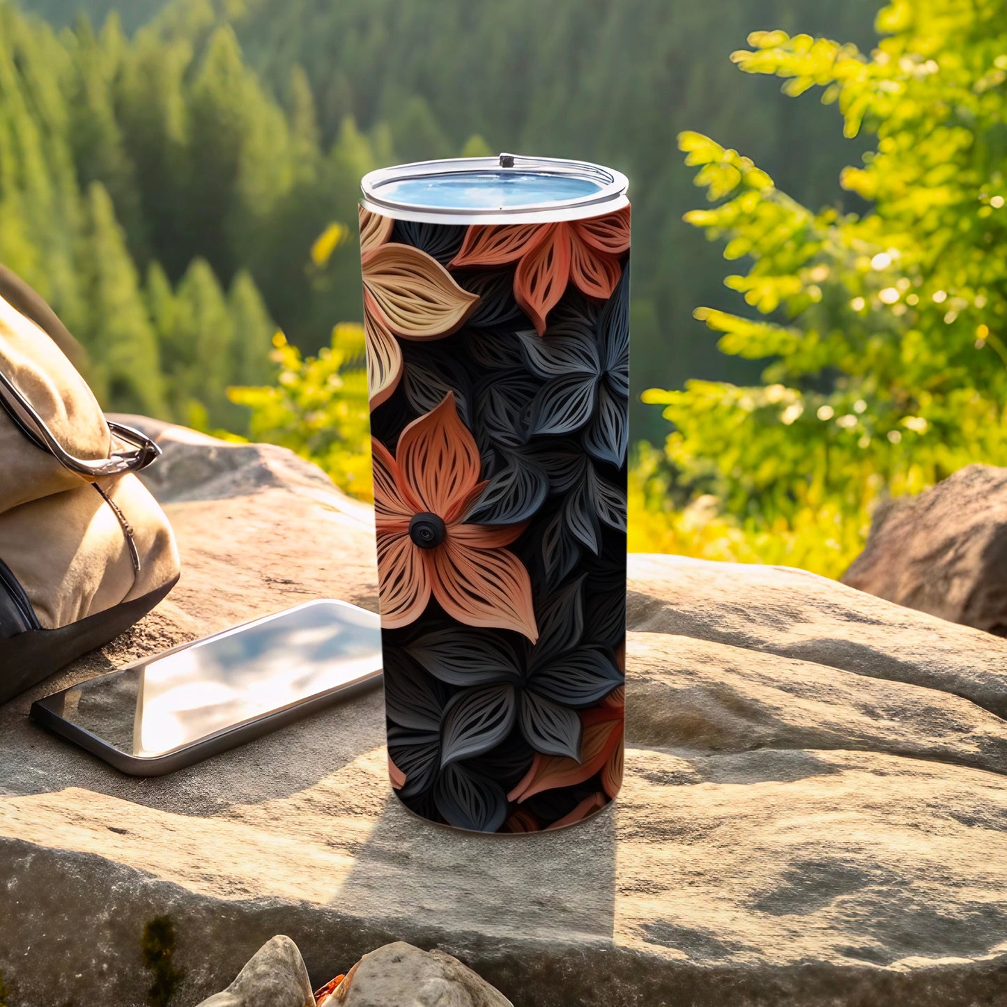 Tall floral patterned tumbler on rock with phone and backpack.