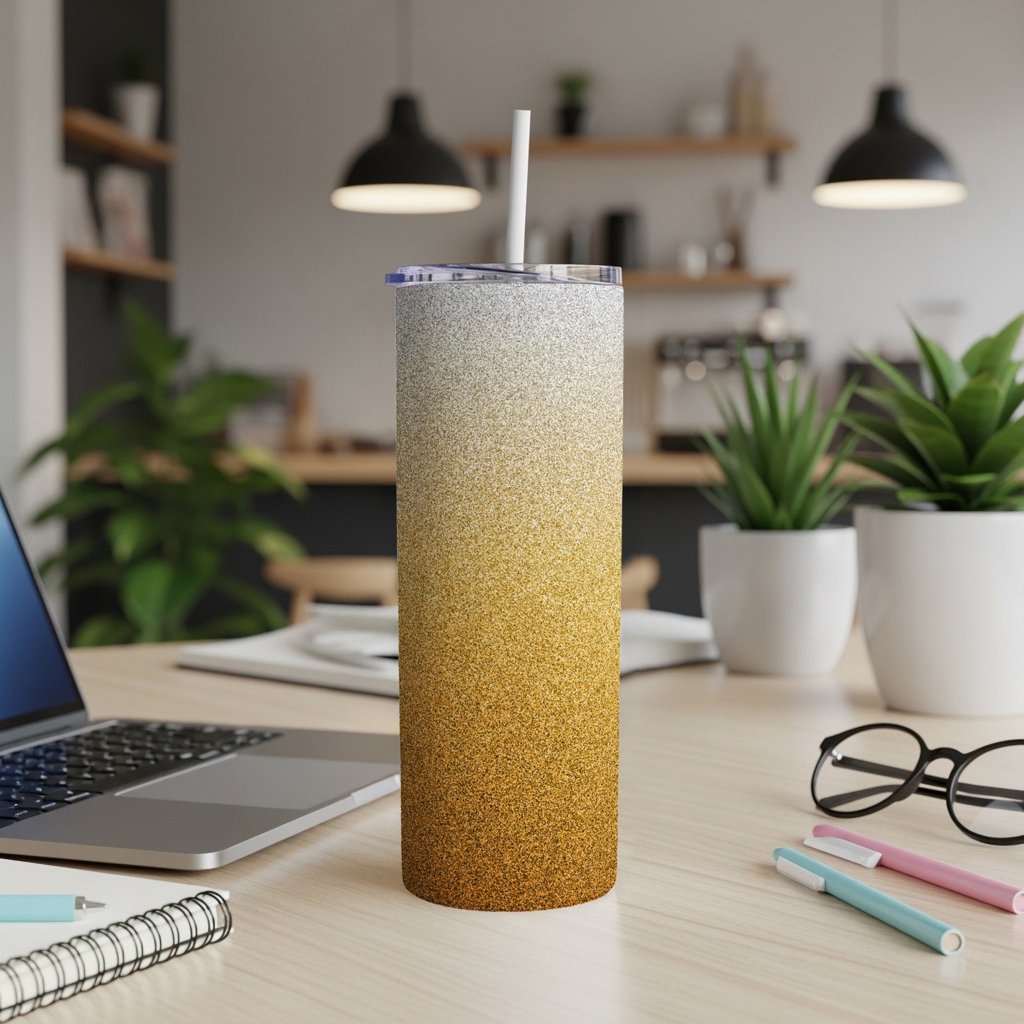 Glitter gradient tumbler with white straw on a desk with laptop and pens.