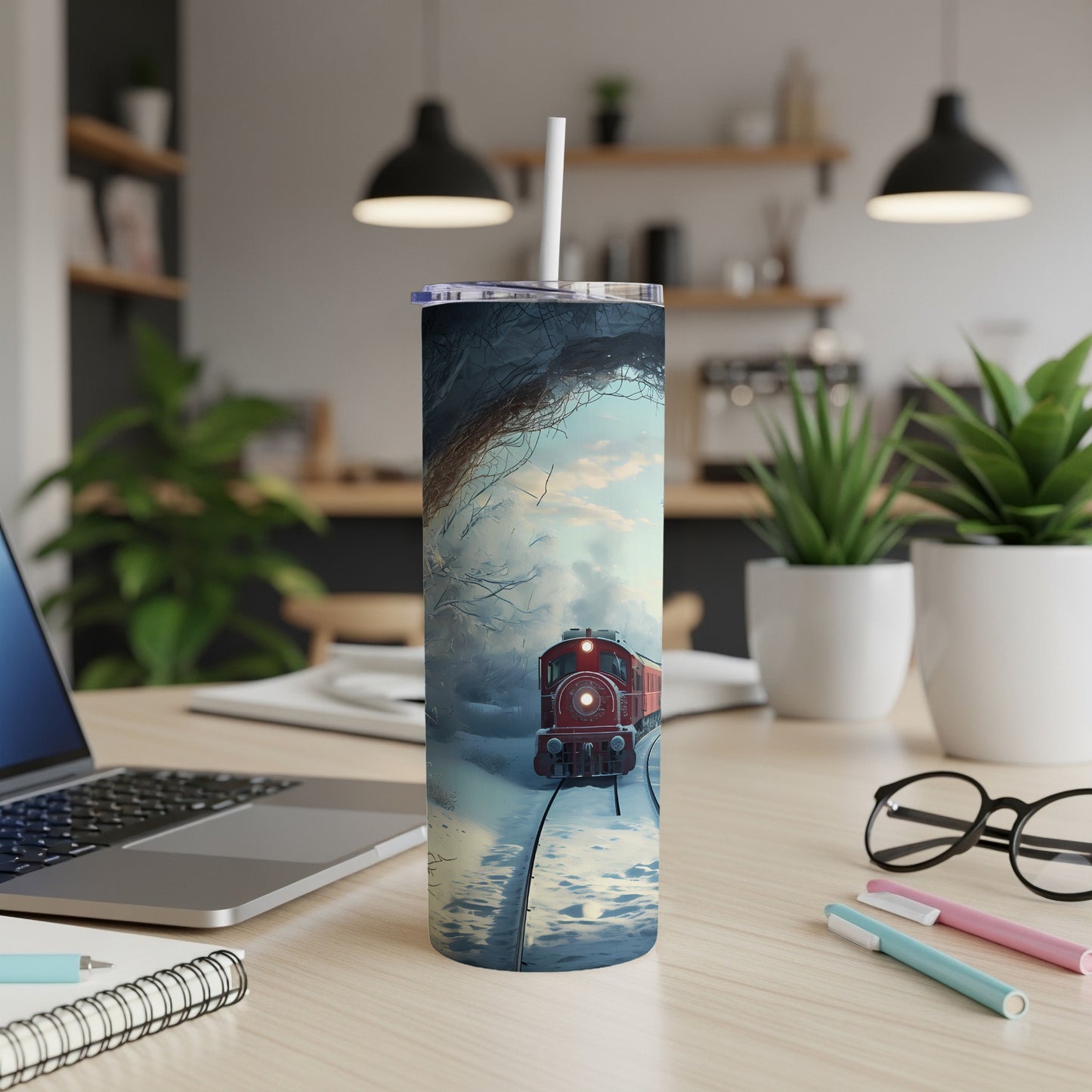 Red train in snowy landscape on a tumbler with straw, viewed on a desk.