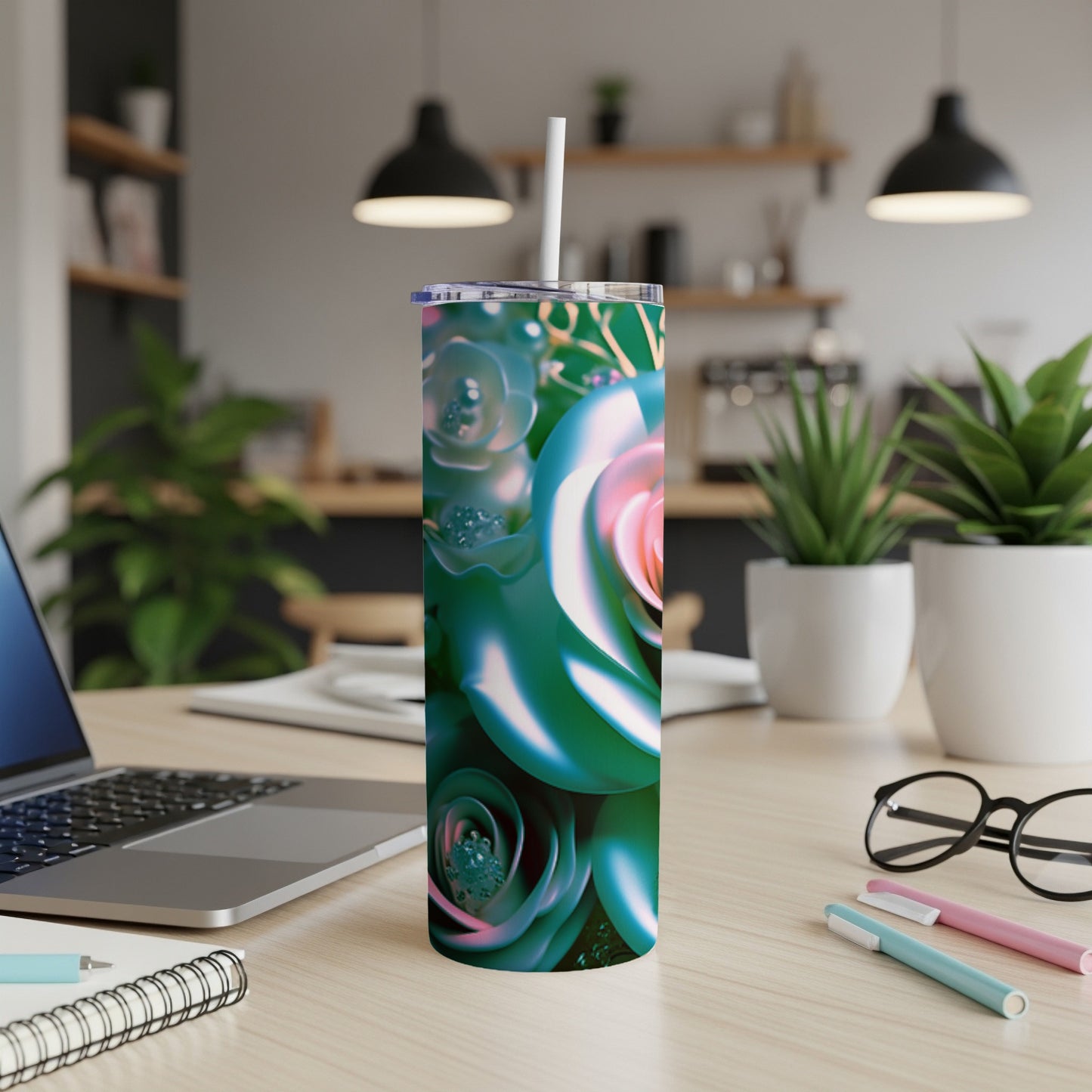 Tall tumbler with teal and pink rose art and straw, on a desk.