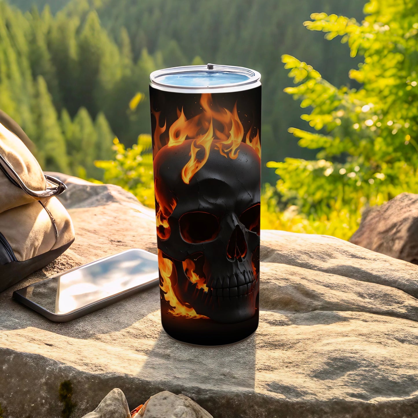 Black skull tumbler with flames, resting on rocks outdoors.