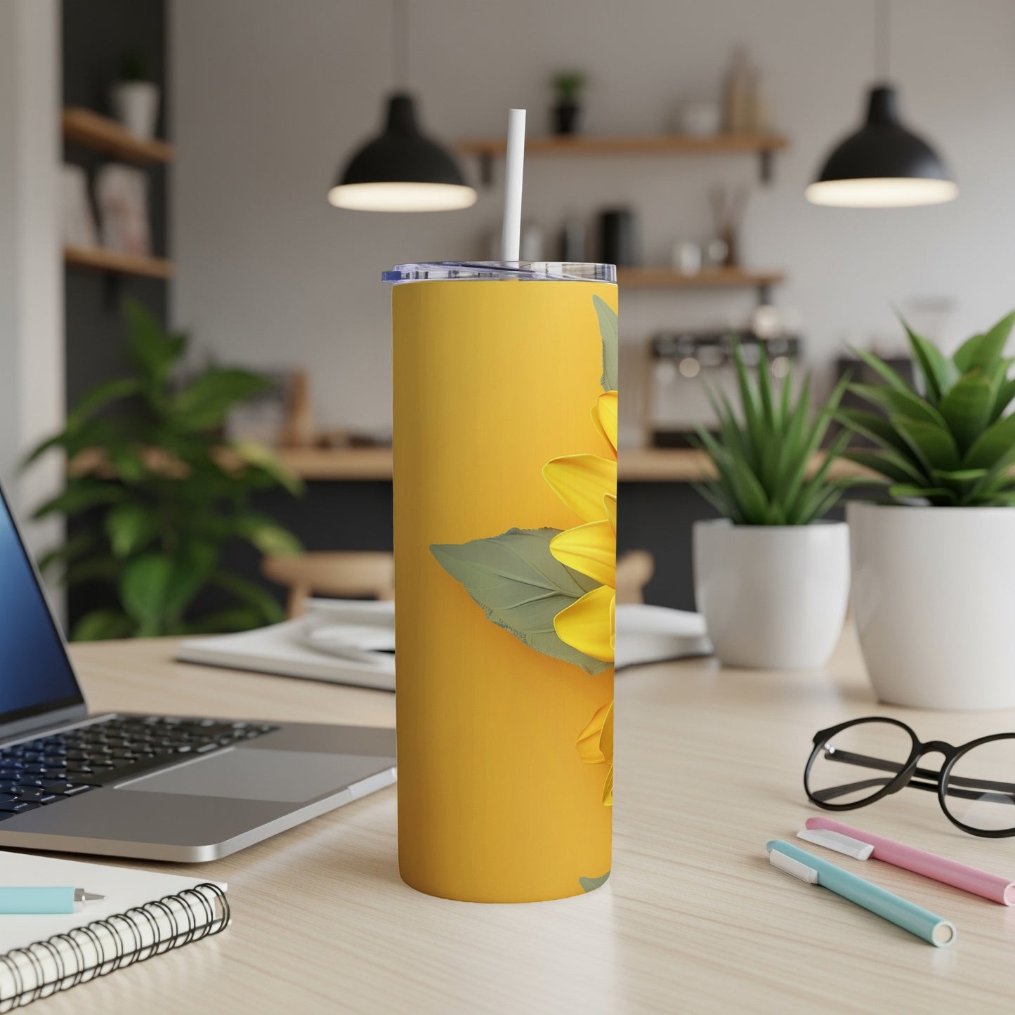 Yellow tumbler with a large sunflower design and white straw on a desk.