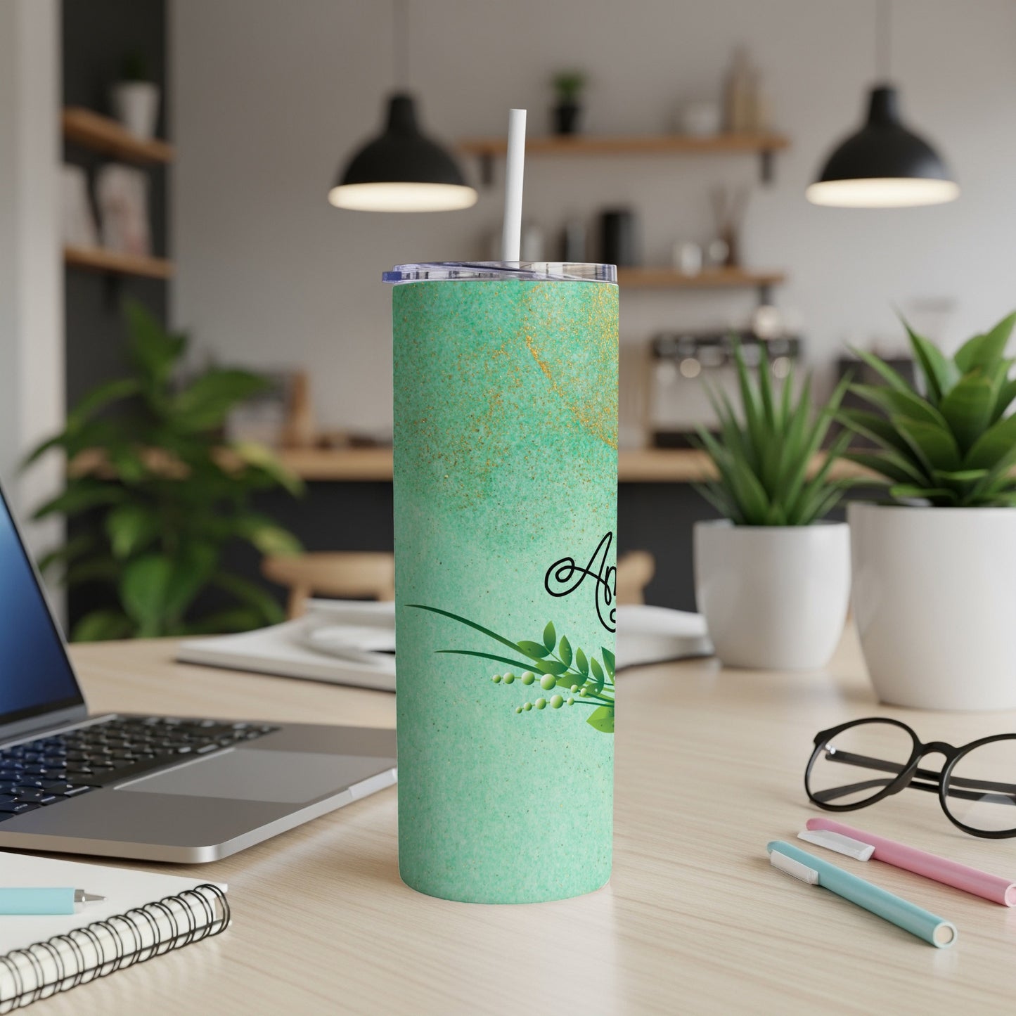 Mint green tumbler with gold flecks and floral design, on a desk.