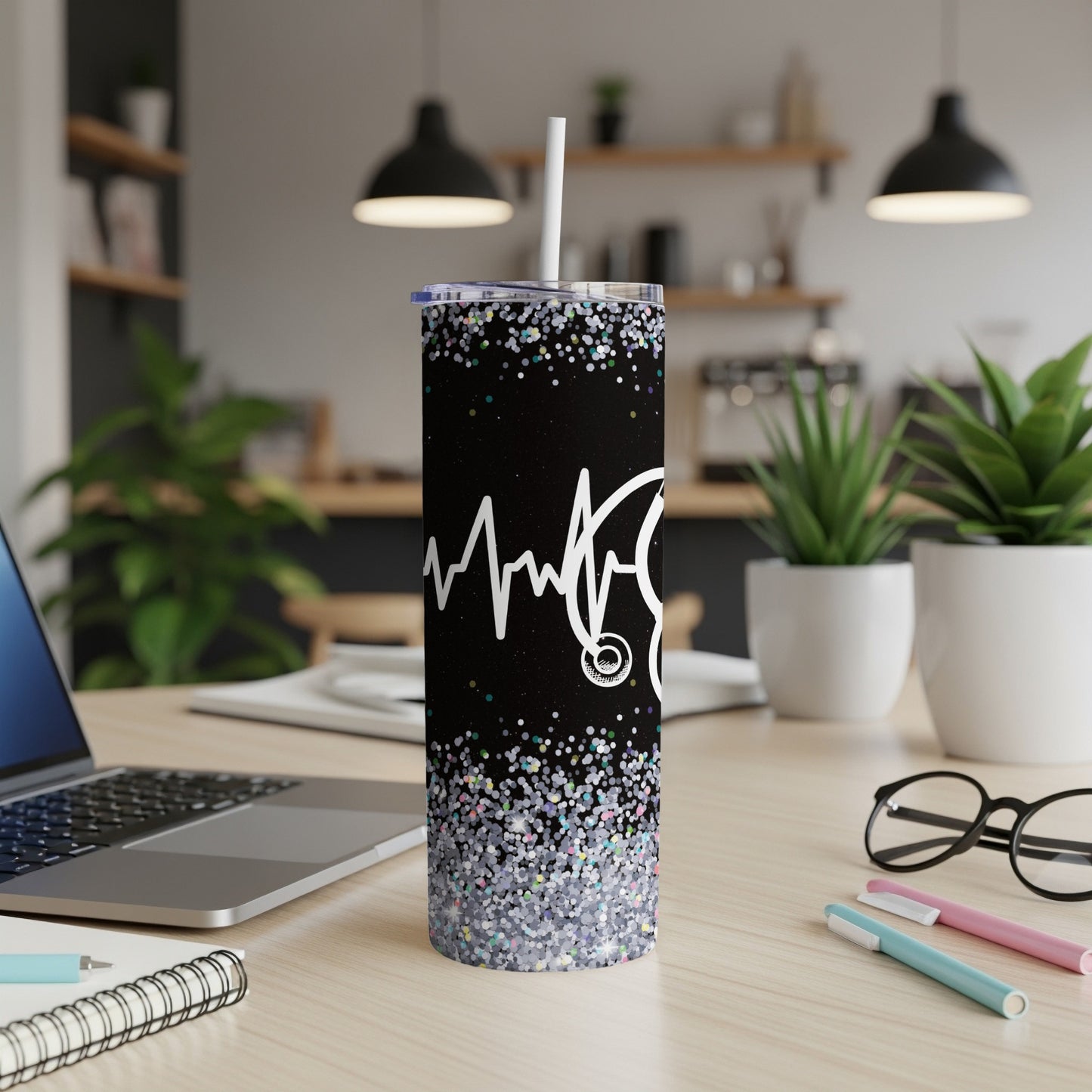 Black tumbler with stethoscope and heartbeat, glitter base, on a desk.
