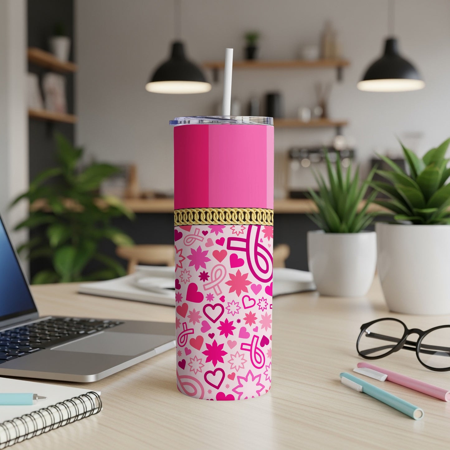 Pink tumbler with ribbon, heart, and star pattern, on a desk with laptop and glasses.