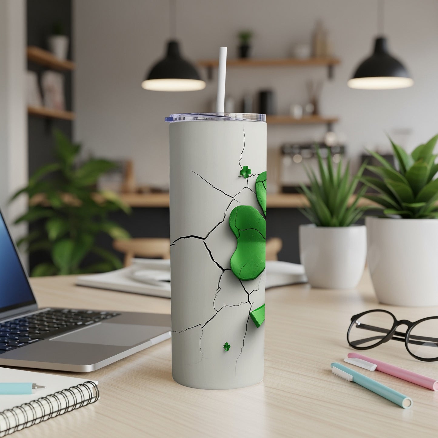 White tumbler with green shamrocks and cracks on a desk.