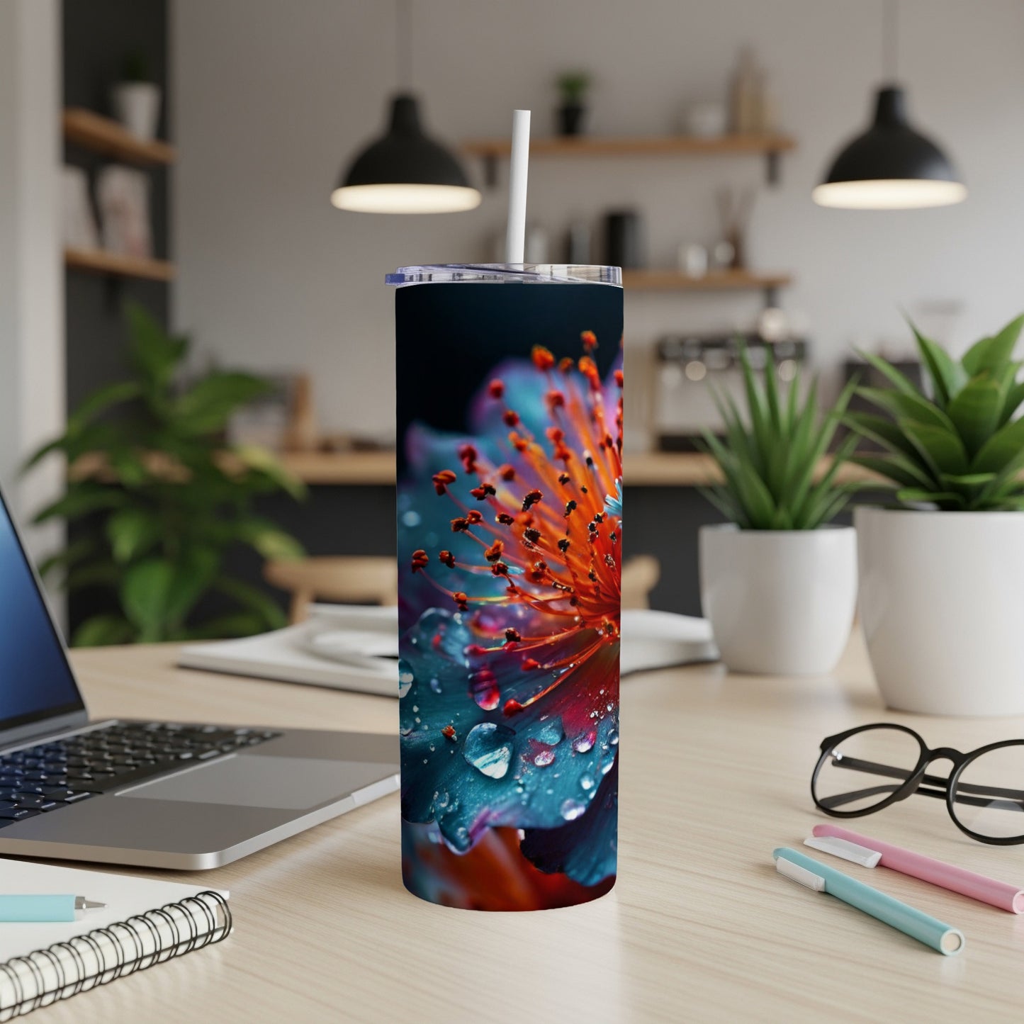 Blue and orange flower with water droplets on a tumbler next to a laptop.