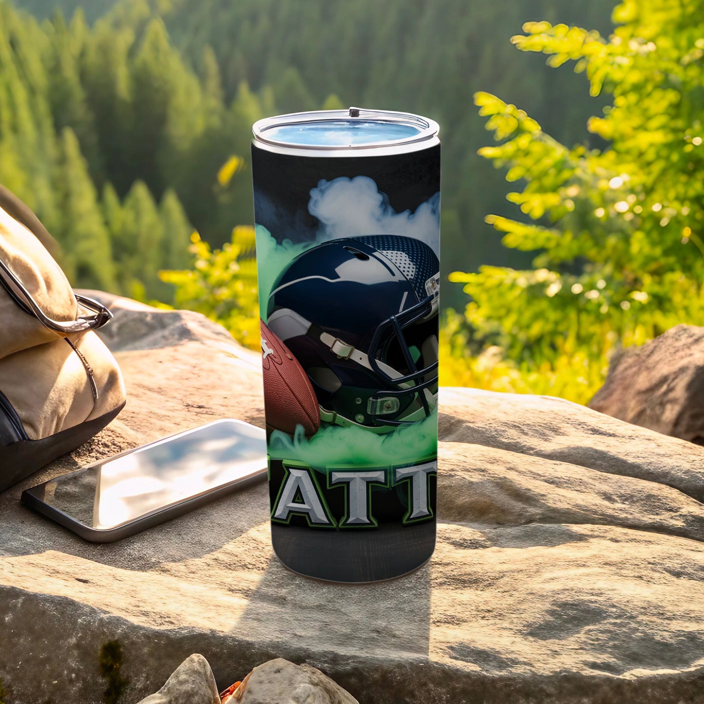 Tumbler with football helmet and "ATTITUDE" text, outdoors with phone and backpack.