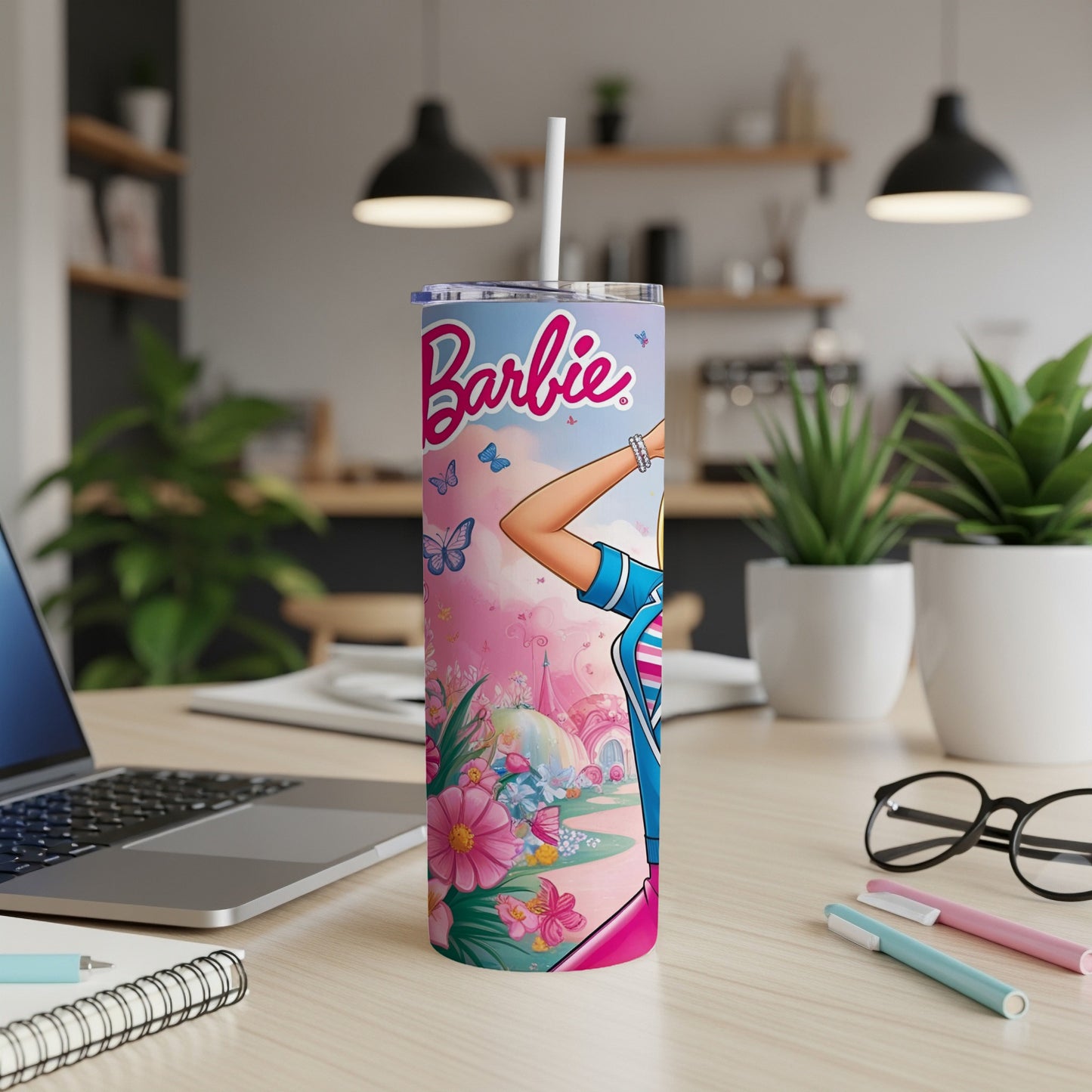 Barbie tumbler with butterflies and flowers, on a desk with laptop and pens.