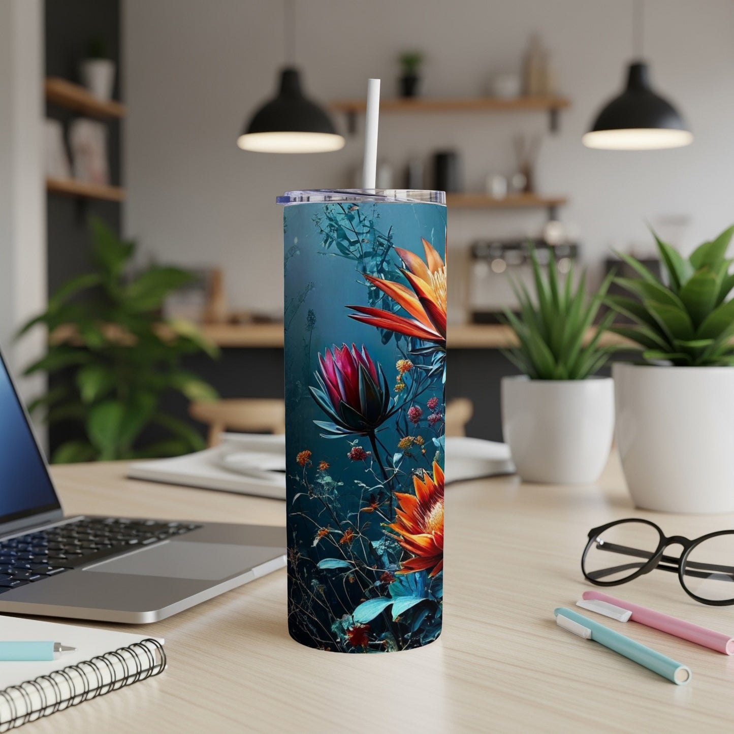 Floral tumbler with straw on a desk with a laptop and pens.