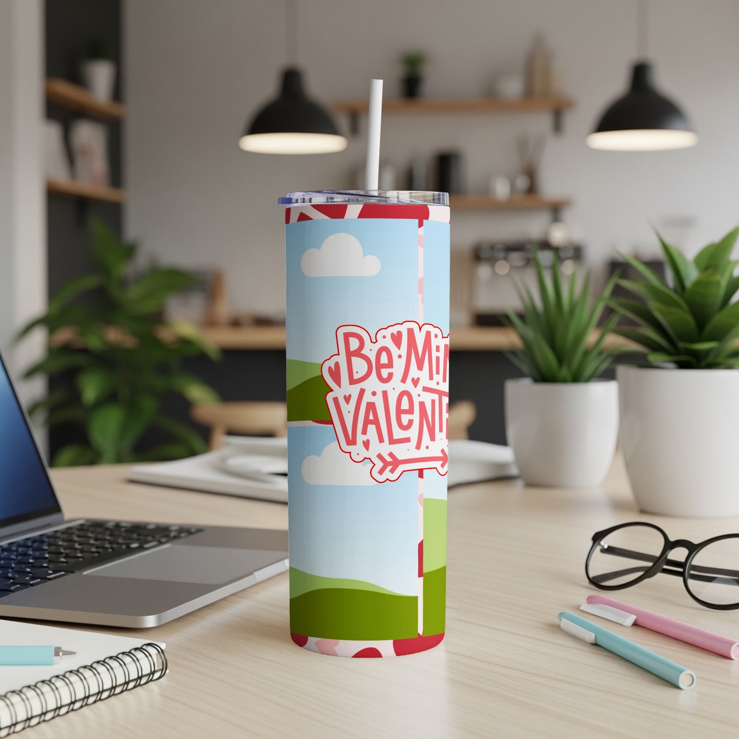 "Be My Valentine" tumbler with a straw on a desk next to a laptop and glasses.