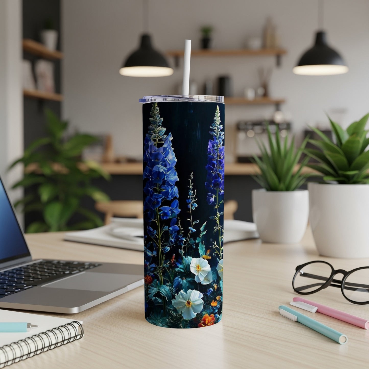 Tall tumbler with blue wildflowers and green leaves on dark background.