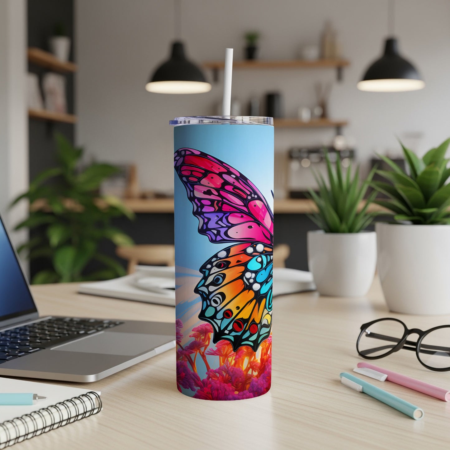 Tall tumbler with colorful butterfly design on desk with laptop and pens.