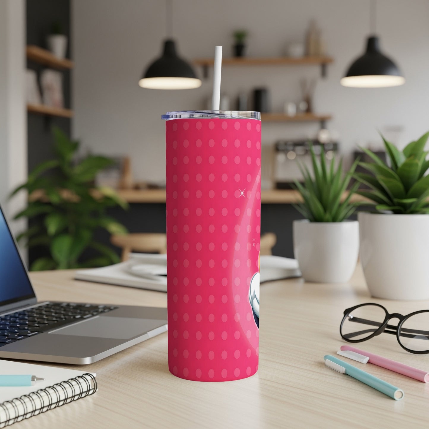 Pink tumbler with white polka dots, straw, on a desk.