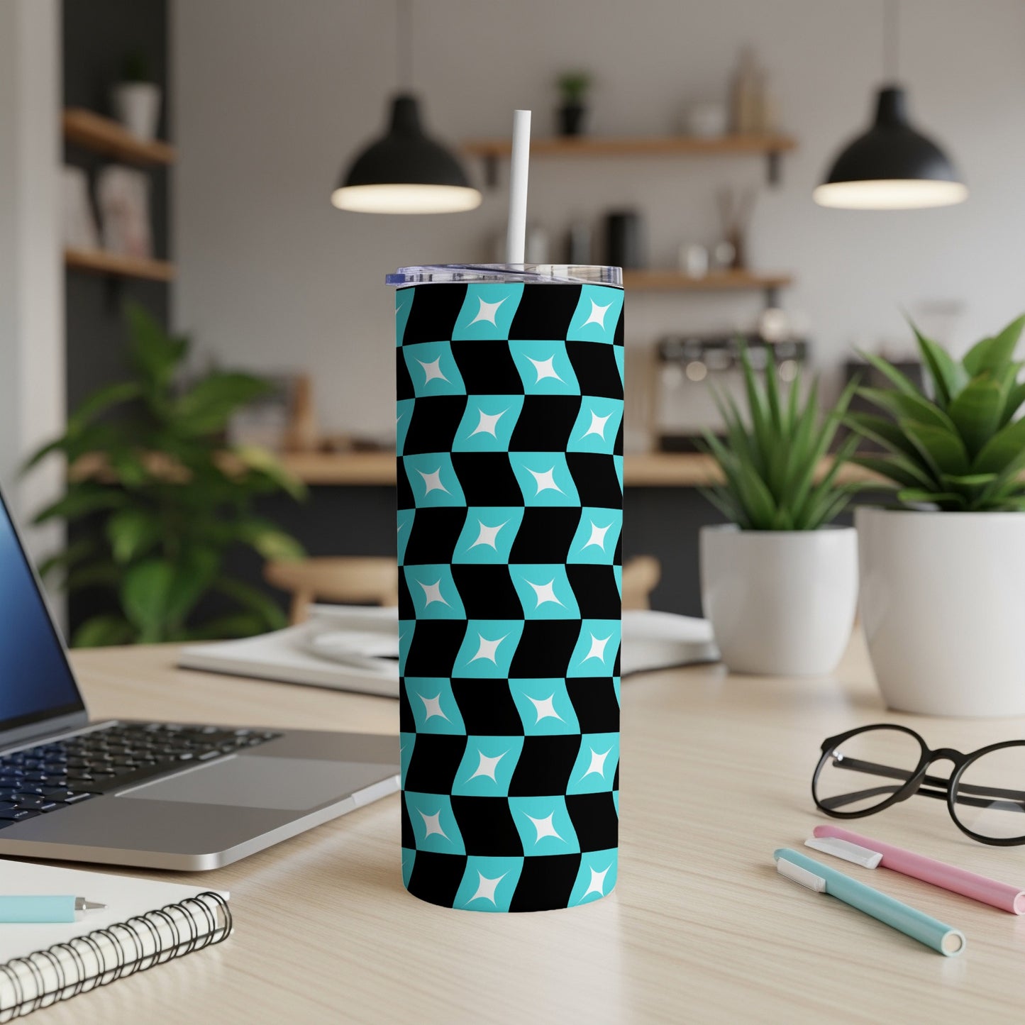 Black, blue, and white geometric pattern skinny tumbler with straw on desk.