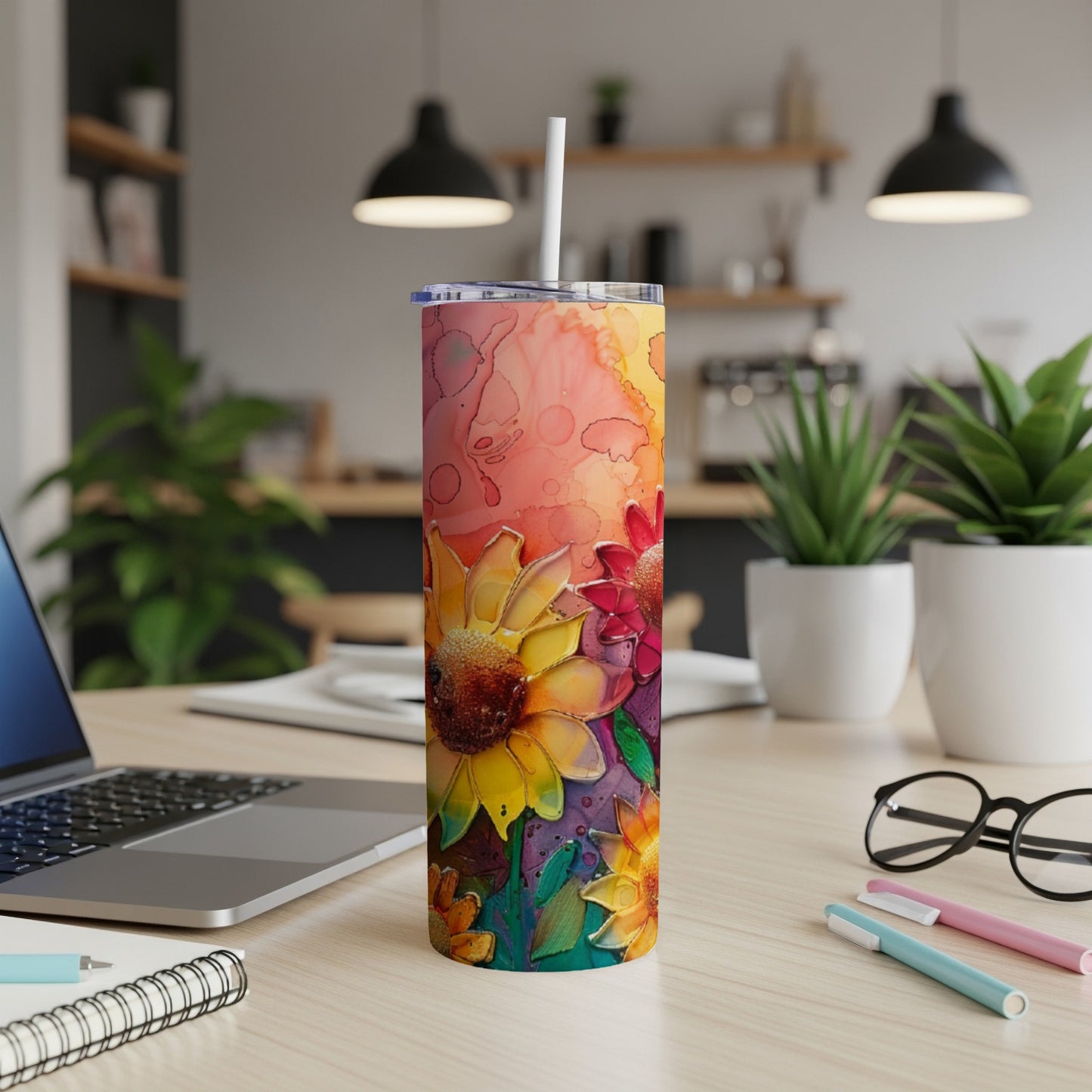 Floral tumbler with straw on a desk with a laptop and pens.