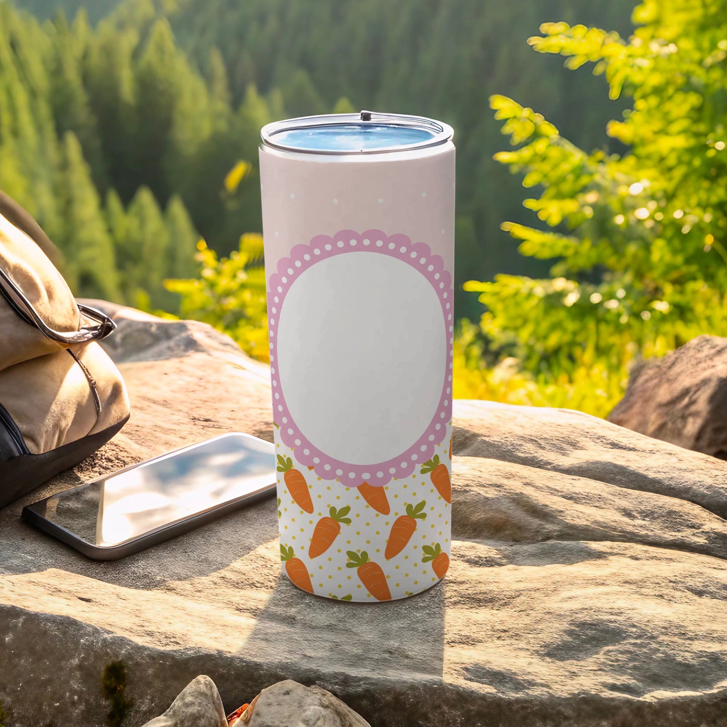 Pink polka dot tumbler with carrots, resting on rocks with a backpack and phone.