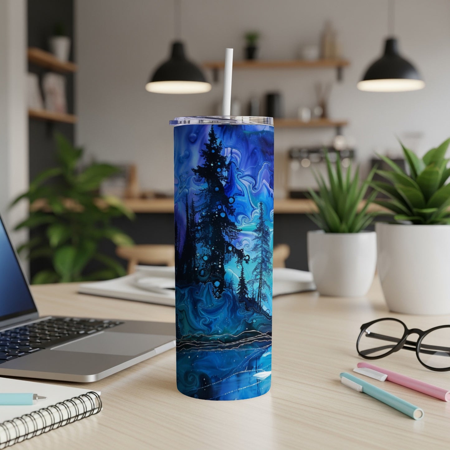 Blue abstract forest scene tumbler with white lid and straw on a desk.