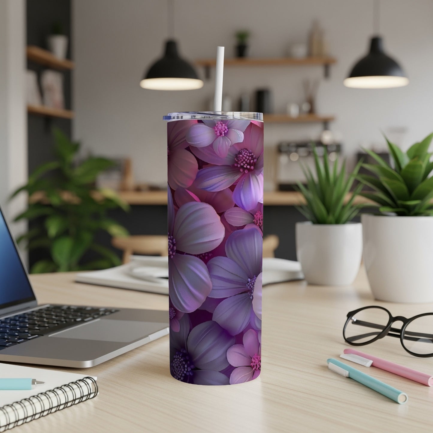 Purple floral tumbler with white straw on a desk next to a laptop and pens.