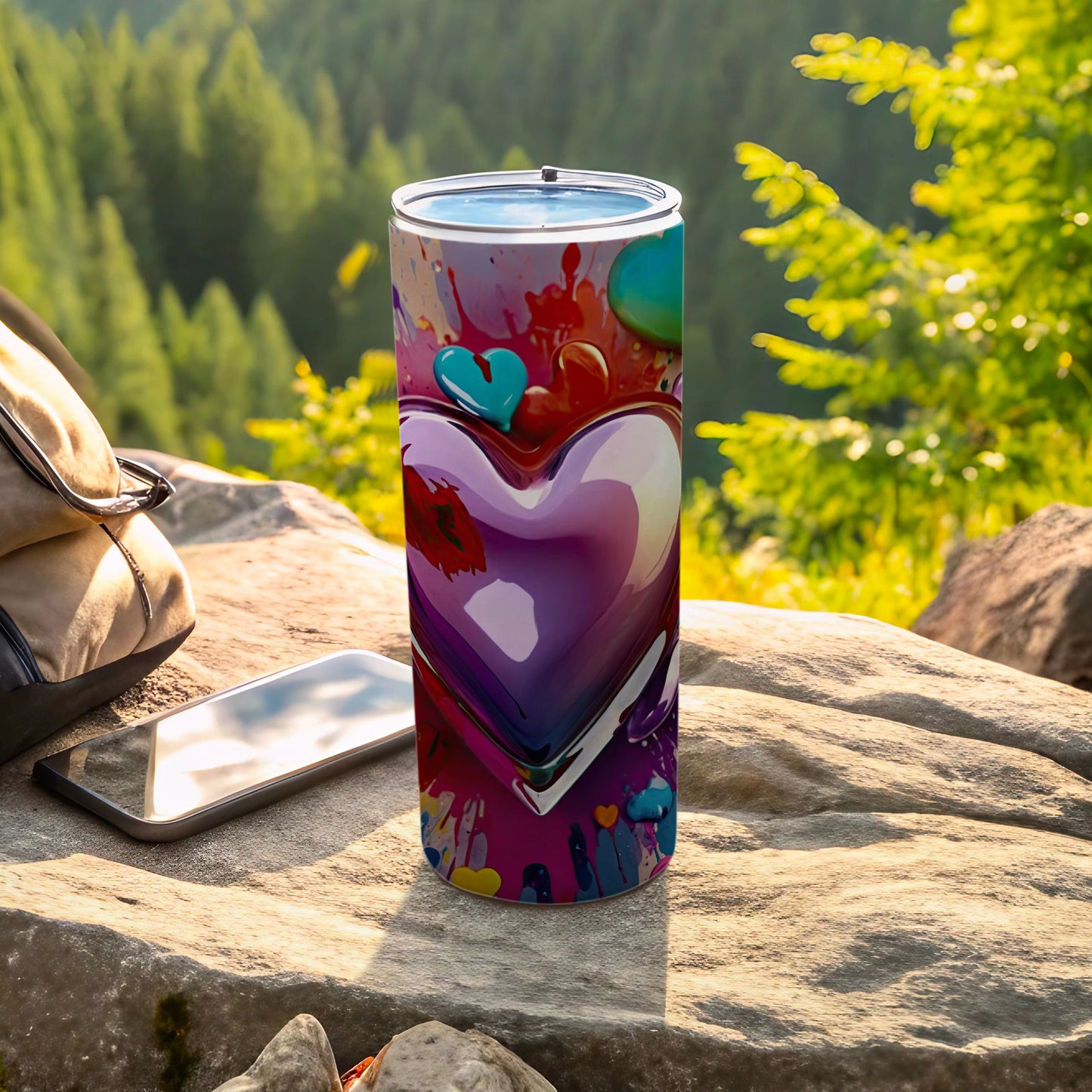 Tumbler with colorful hearts, phone, and bag on rock, outdoors.