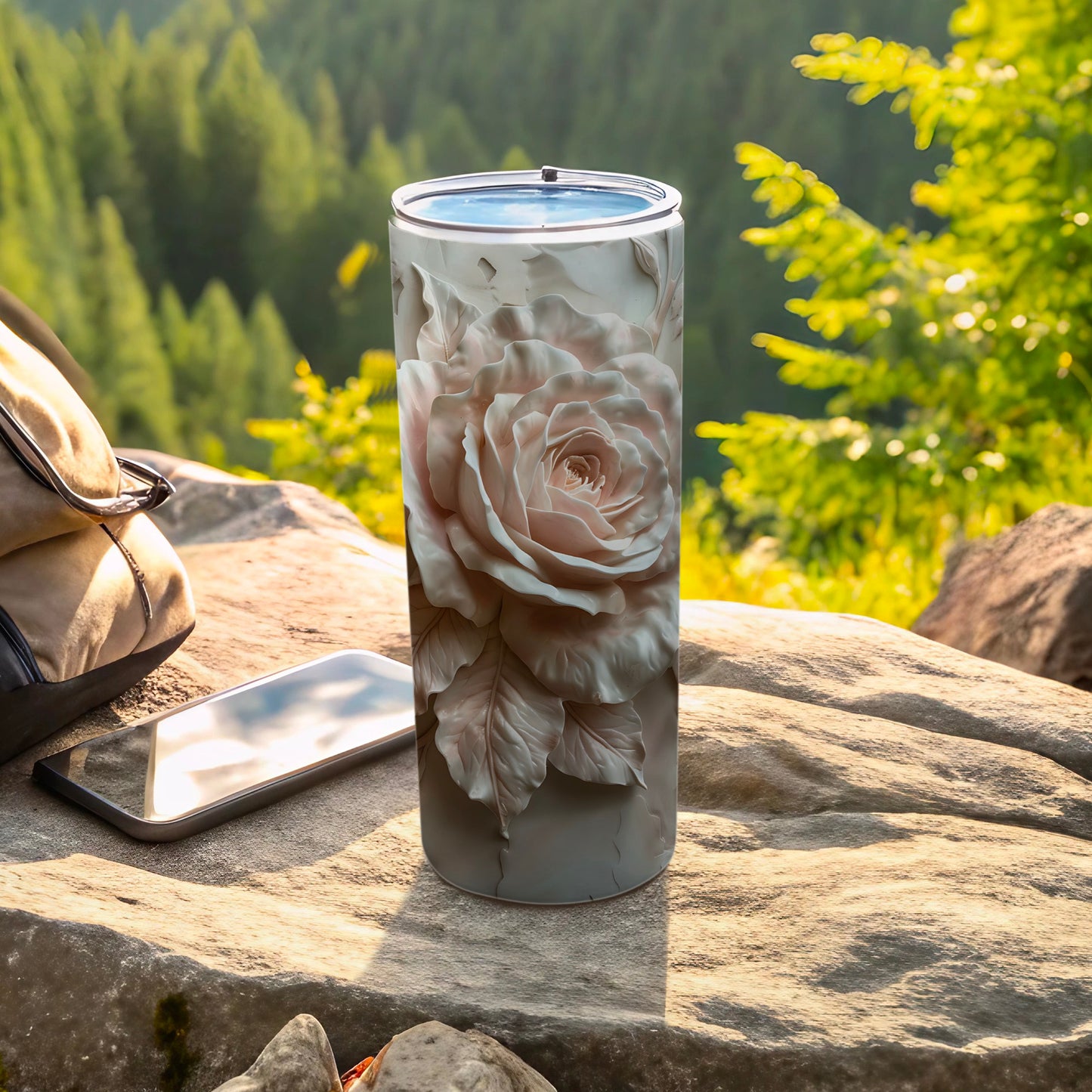 Tall tumbler with intricate light pink rose design, beside a phone and backpack.