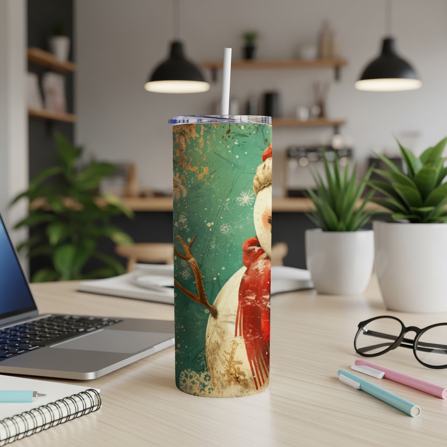 Snowman tumbler with straw on a desk with laptop and pens.