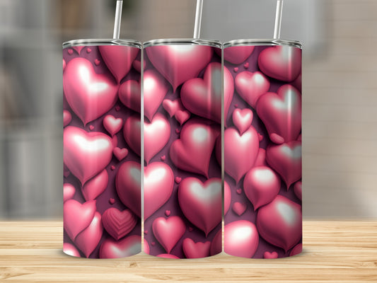 Three pink heart-patterned tumblers with straws on a wooden surface.