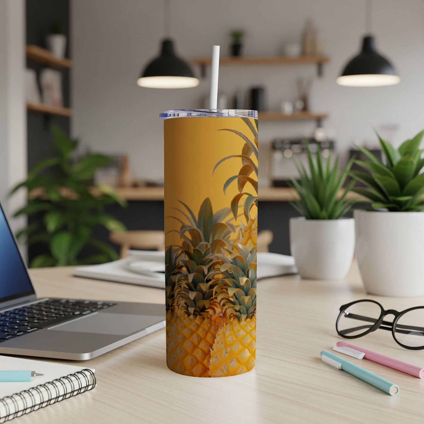 Yellow tumbler with pineapple print on desk with laptop and pens.