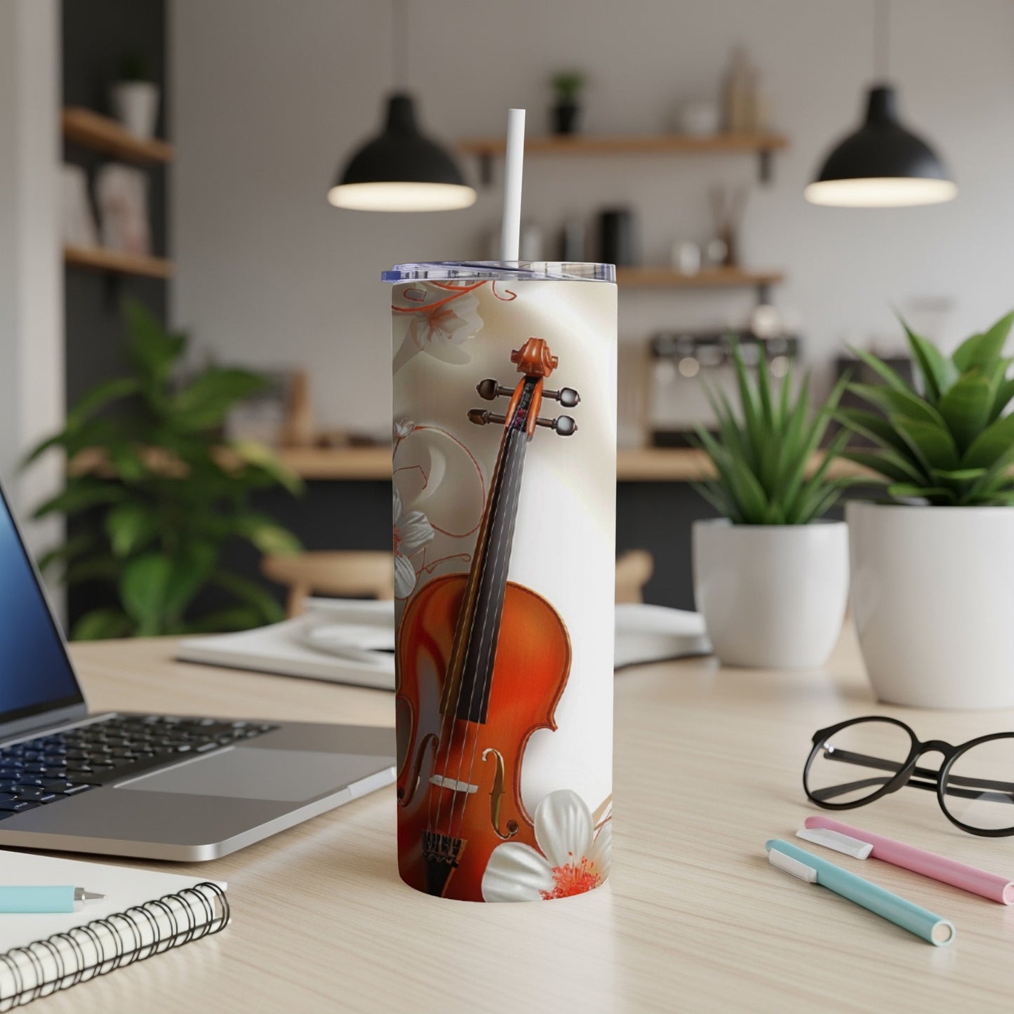Violin with floral design on a white tumbler with straw, on a desk.