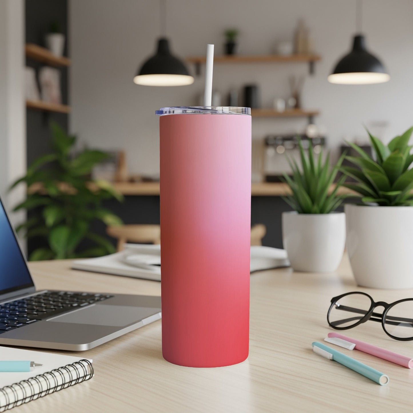 Pink gradient tumbler with straw on desk next to laptop.