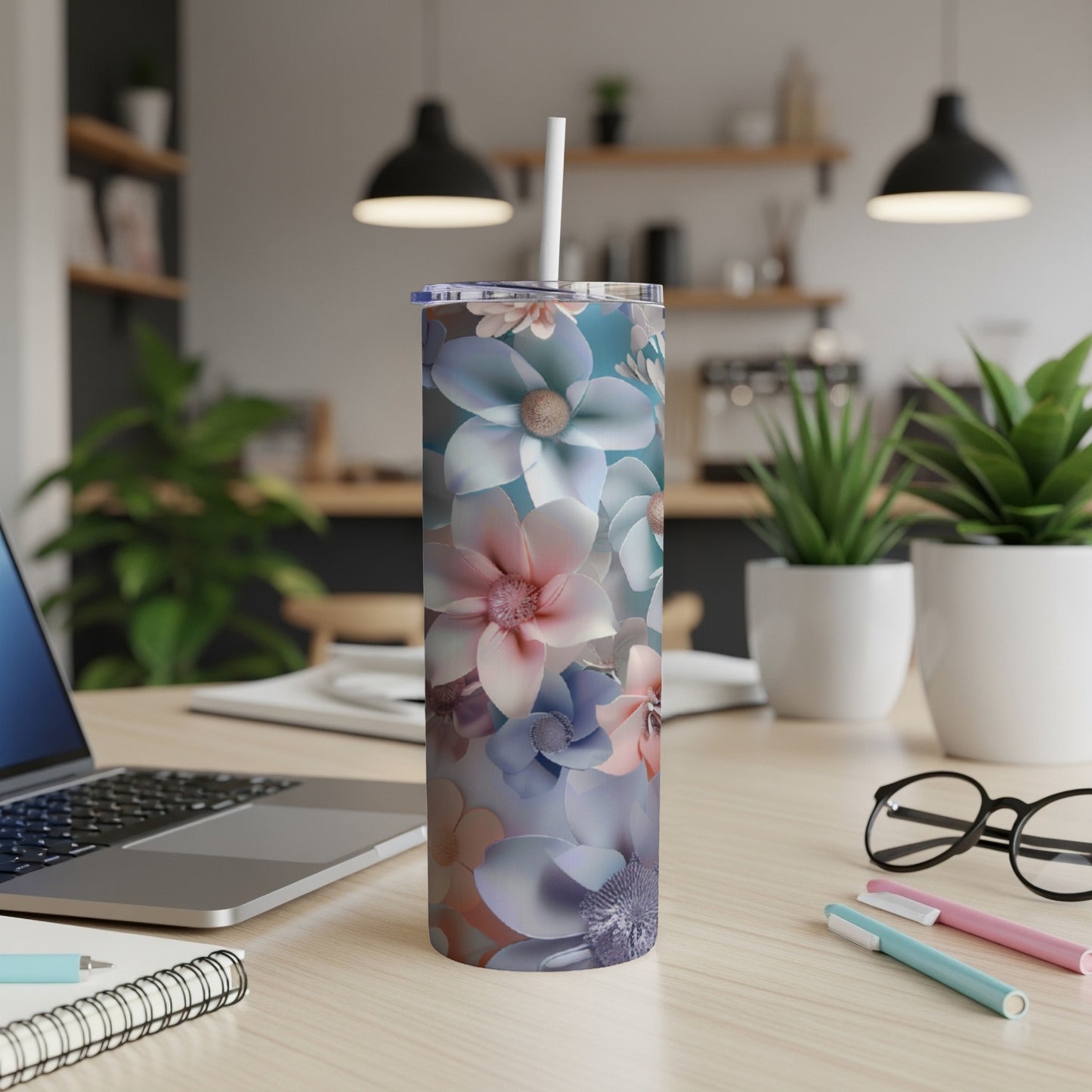 Floral tumbler with straw on a desk with a laptop and pens.