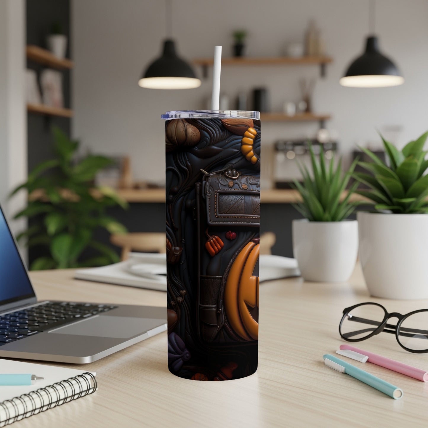 Tumbler with Halloween pumpkin and fall leaf pattern, next to a laptop and notebook.