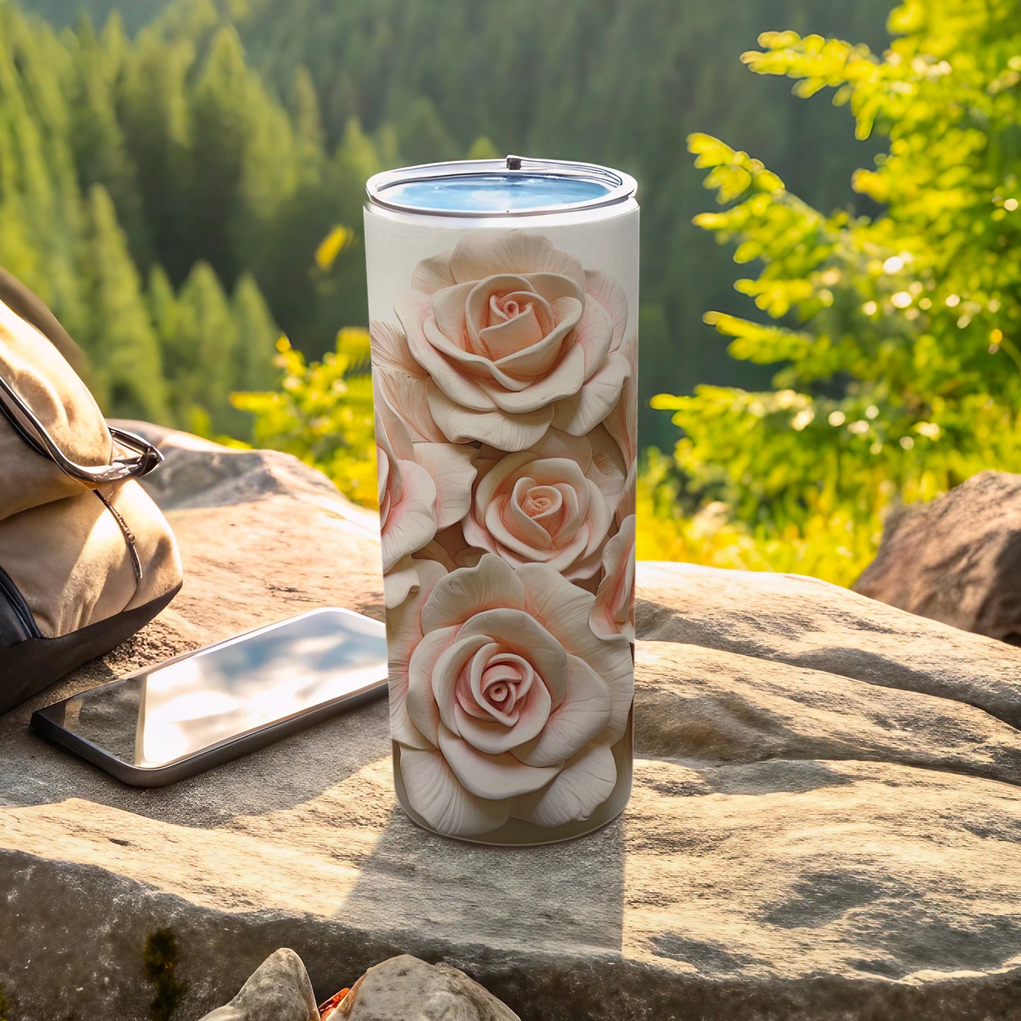 Tall tumbler with delicate pink rose floral design on a rocky outdoor surface.
