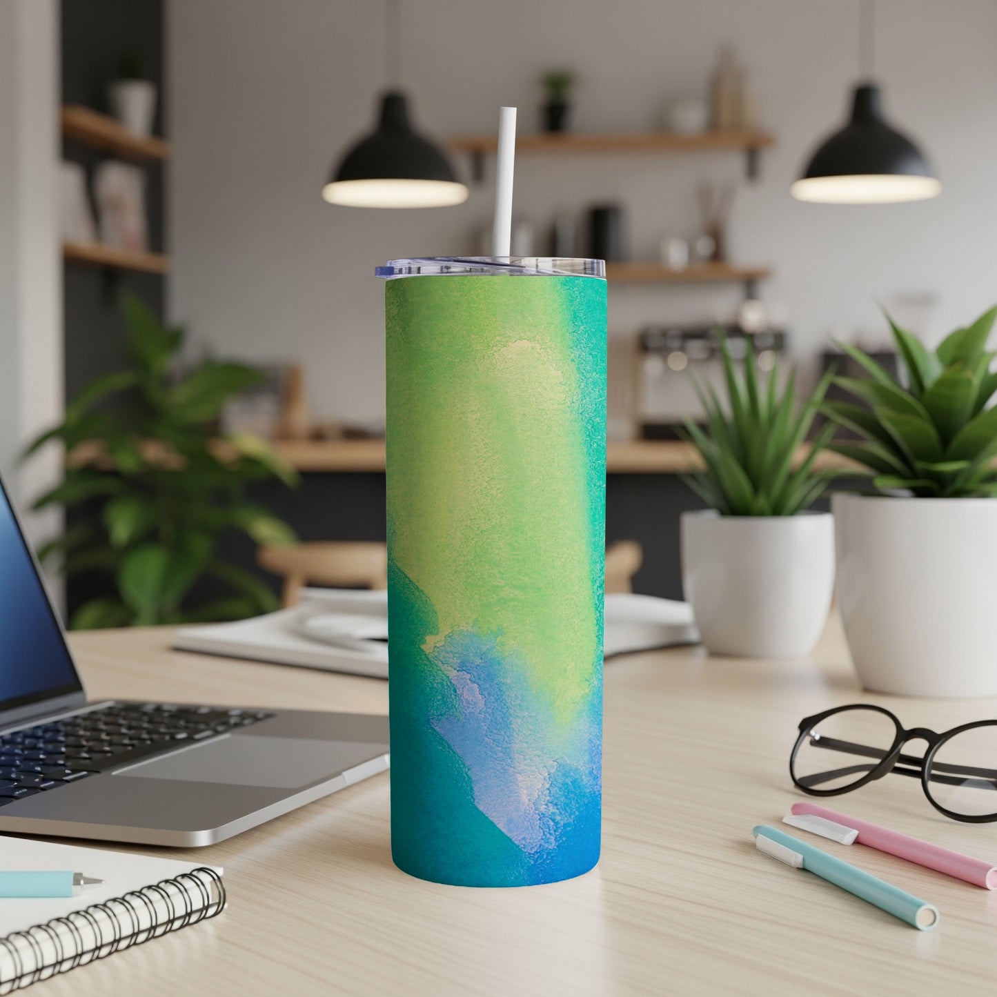 Abstract watercolor tumbler with blue, green, and yellow hues on a desk.