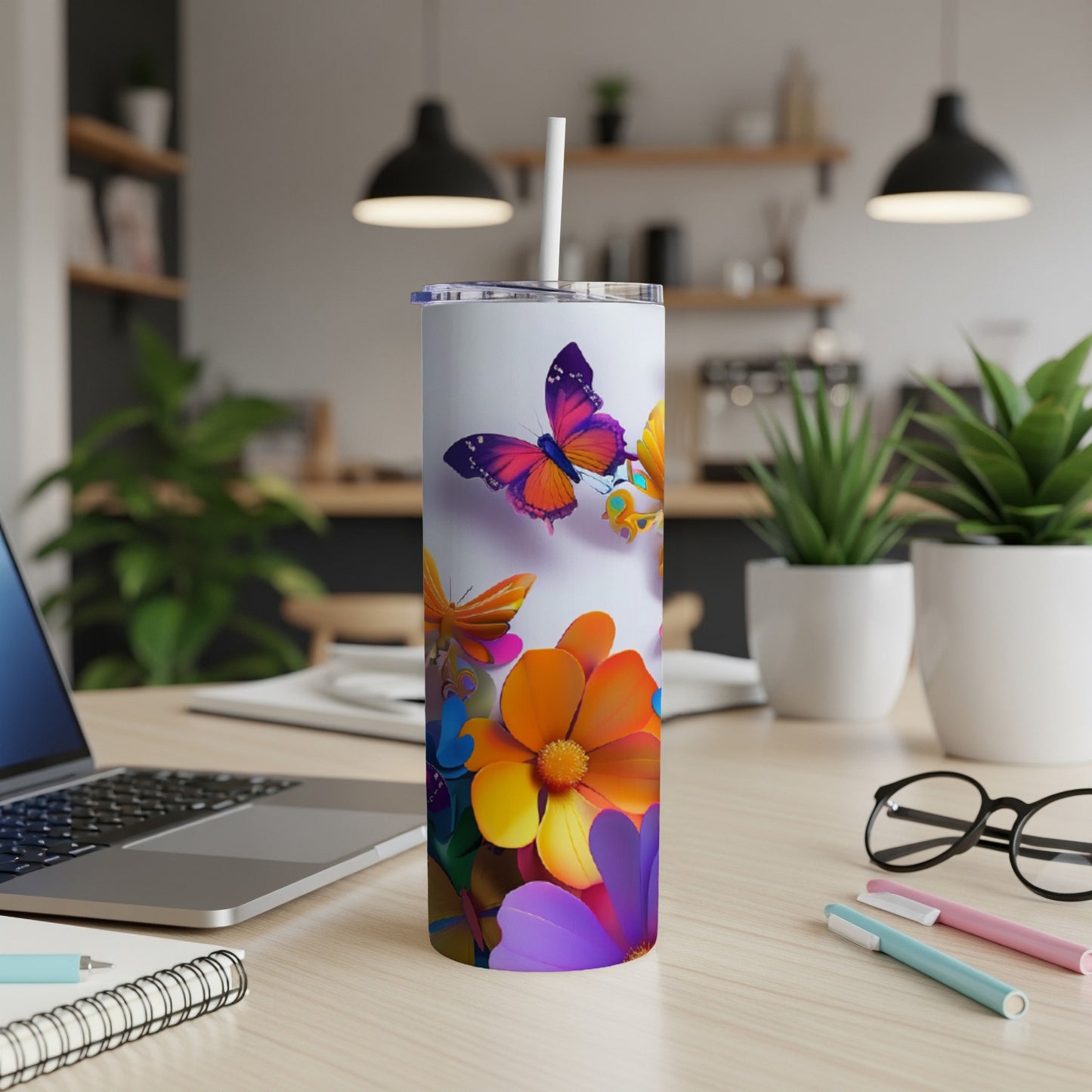 Tall tumbler with colorful flowers and butterflies, on a desk.