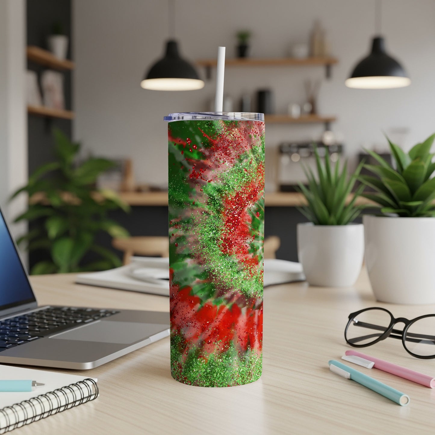 Red and green glitter tumbler with straw on a desk.