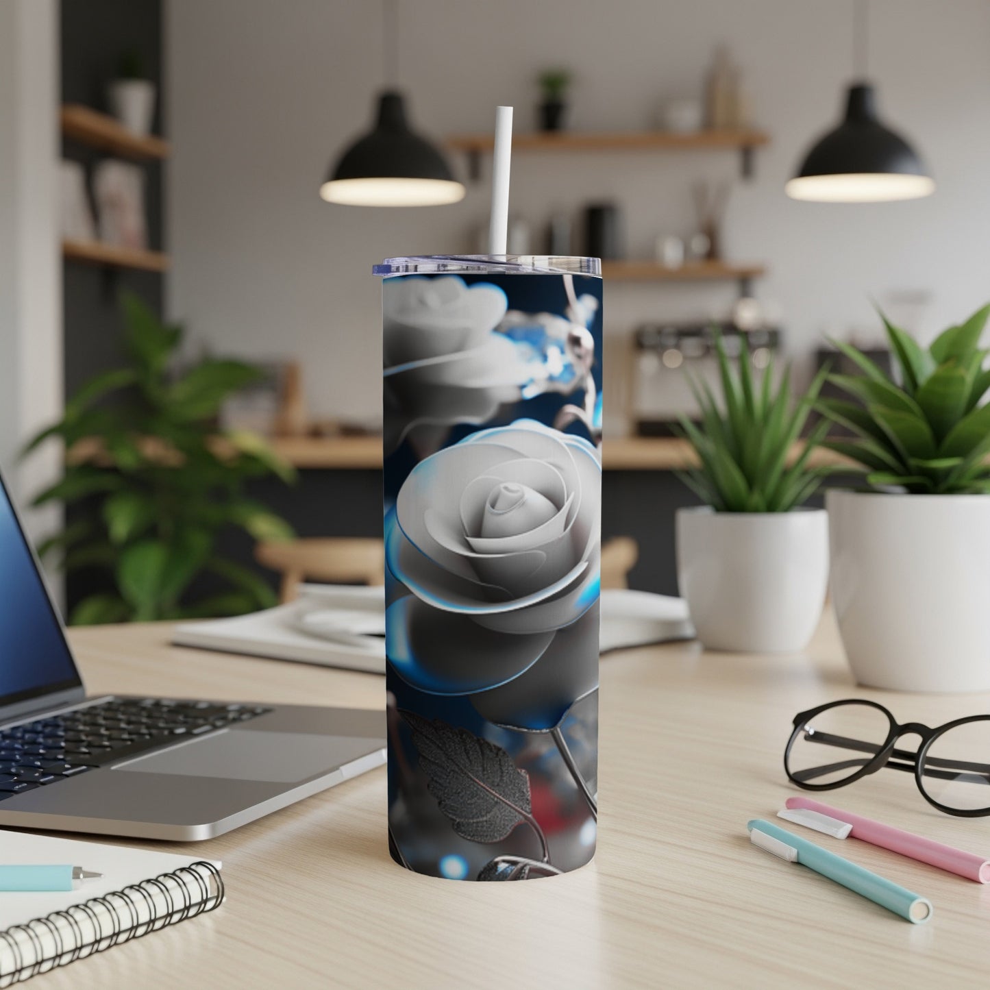 Silver rose tumbler with white straw on a desk with laptop and pens.