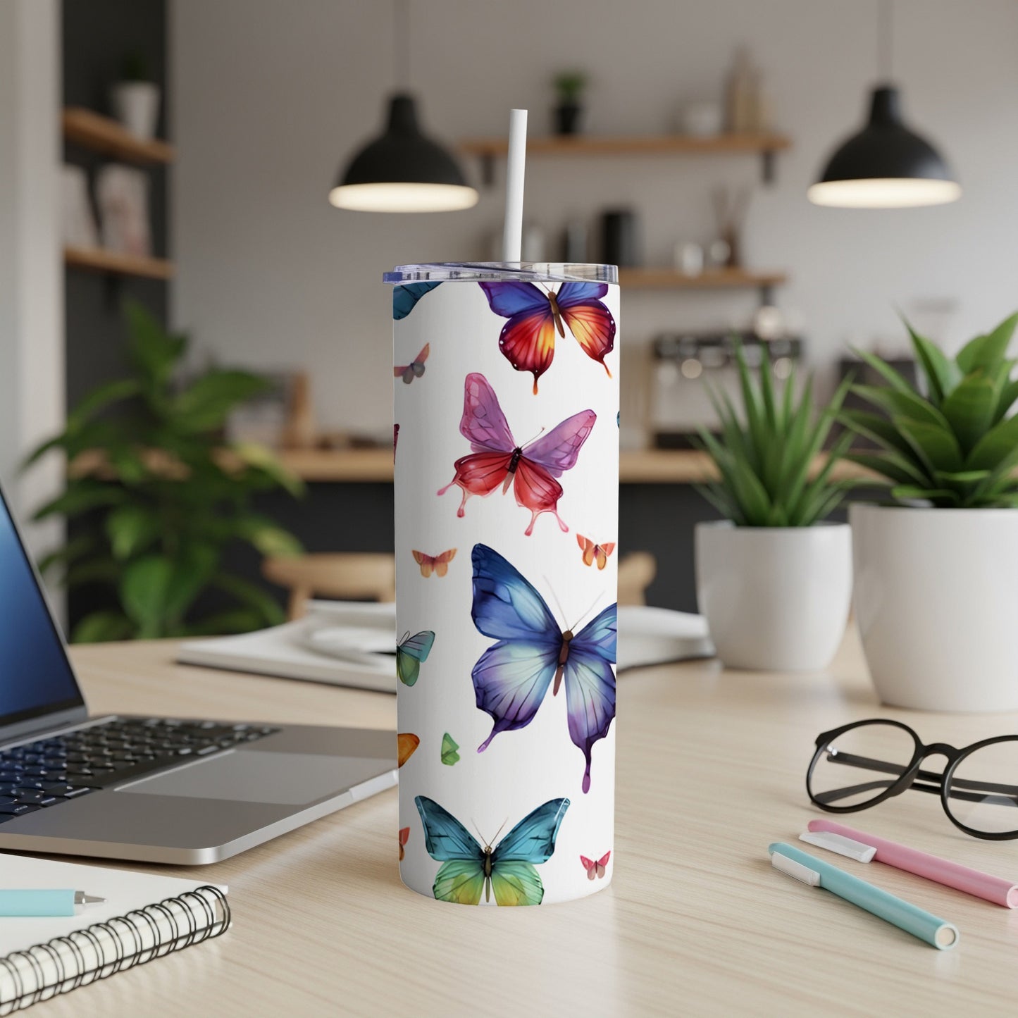 White tumbler with colorful butterflies, lid, and straw on a desk.