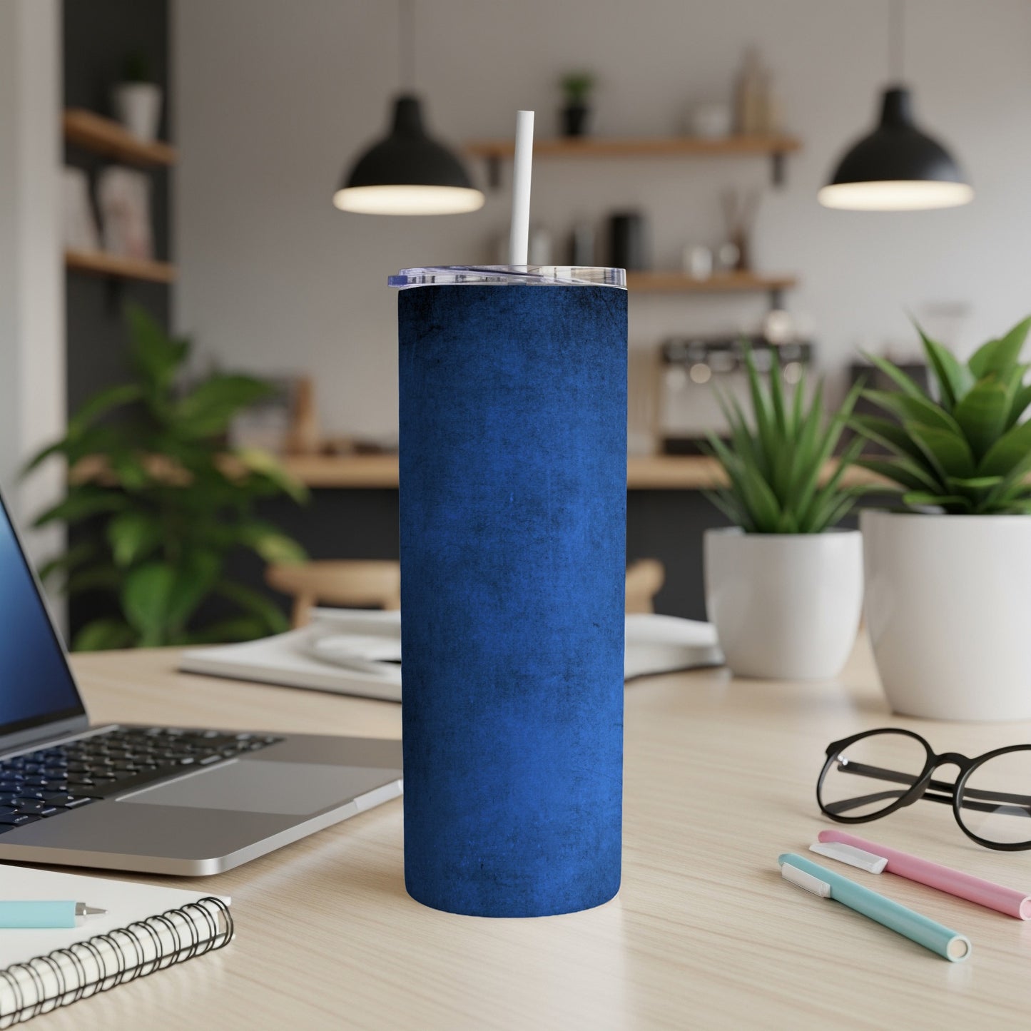 Blue textured tumbler with lid and straw on desk with laptop and plants.