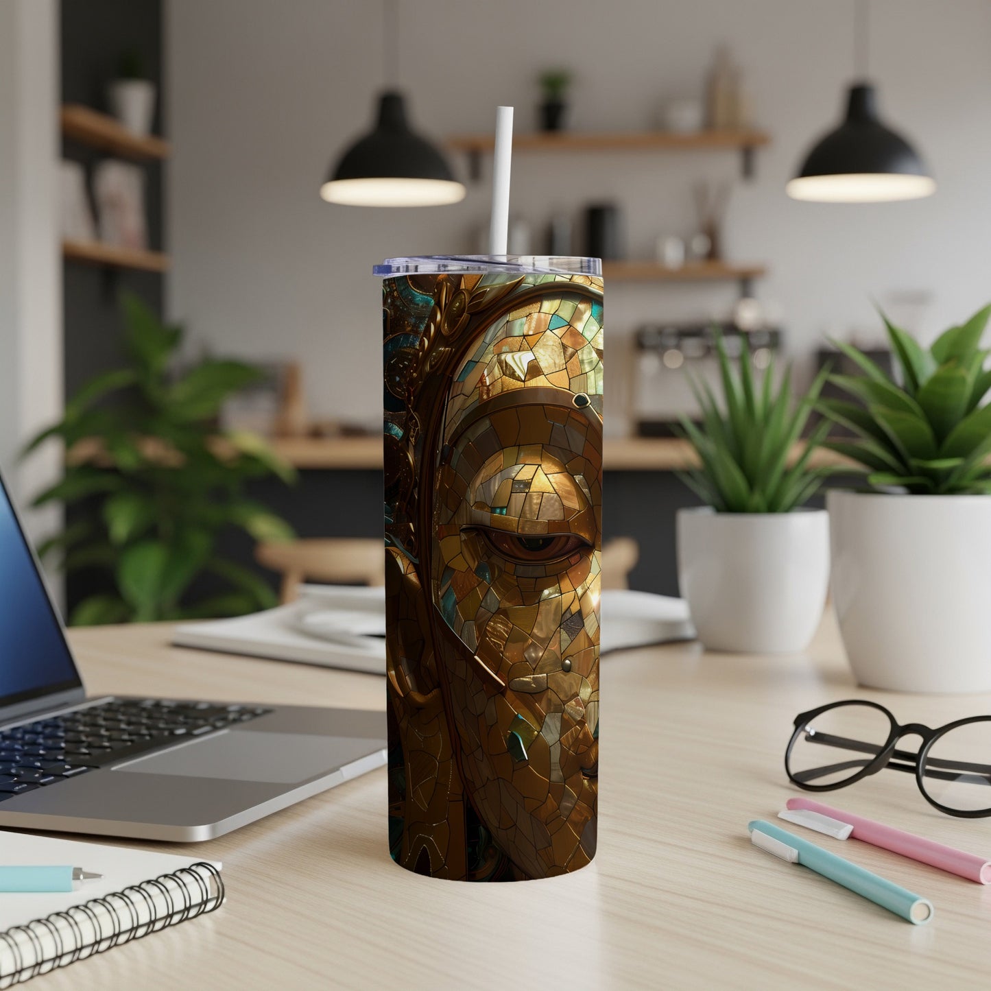 Gold mosaic face on a tumbler with straw, on a desk.