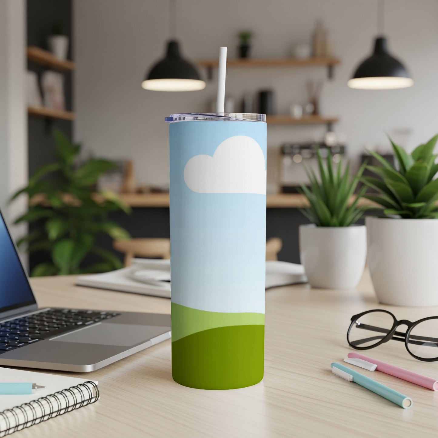 Tall tumbler with a sky and green hills design, featuring a straw.
